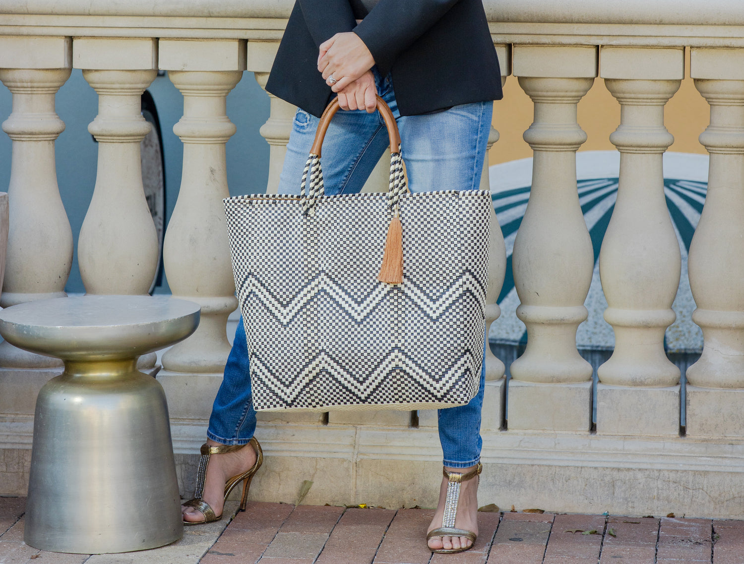 Woman wearing jeans and black blazer holding woven black and white chevron bag