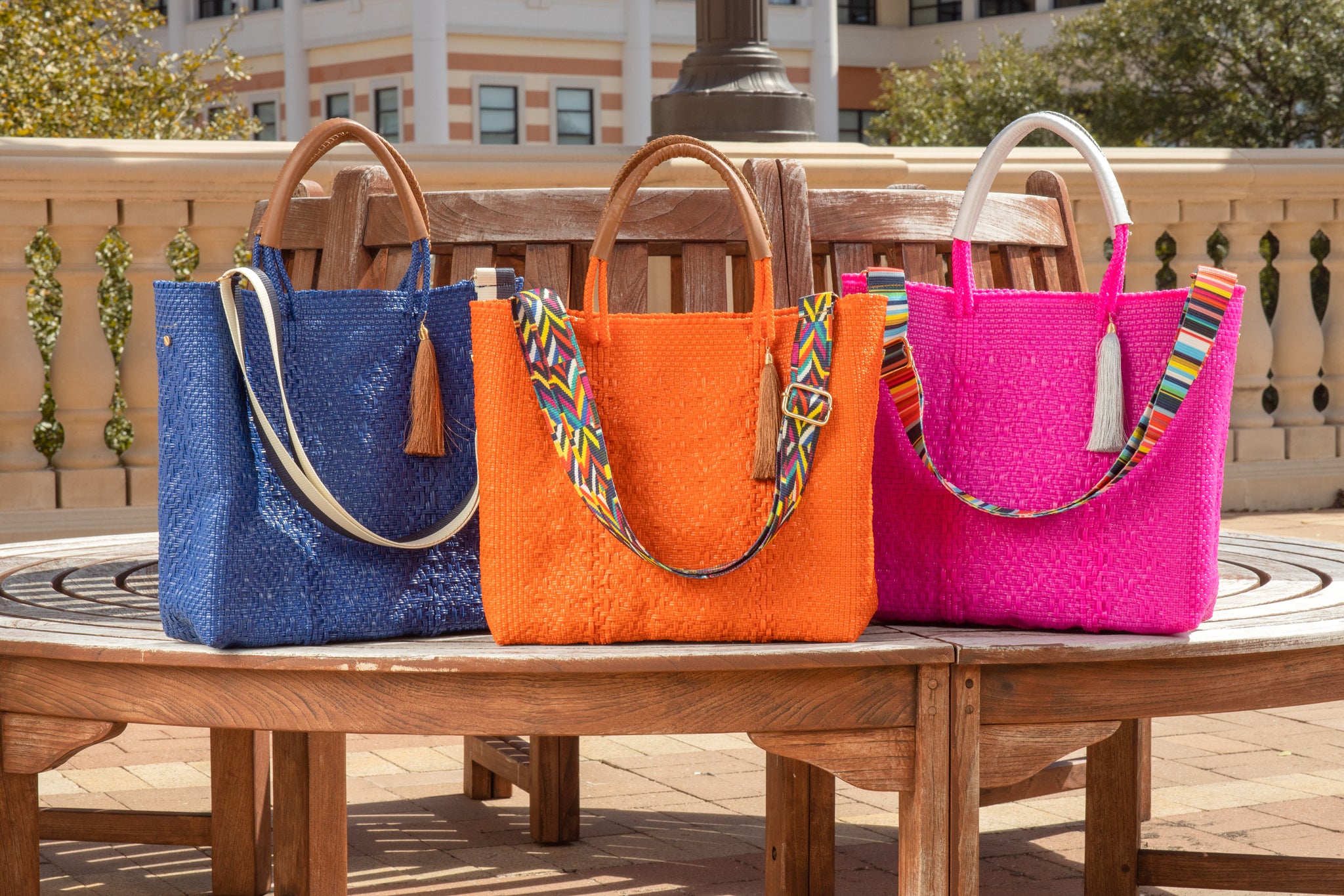 Navy blue, orange, and hot pink handbags with colorful straps on park bench