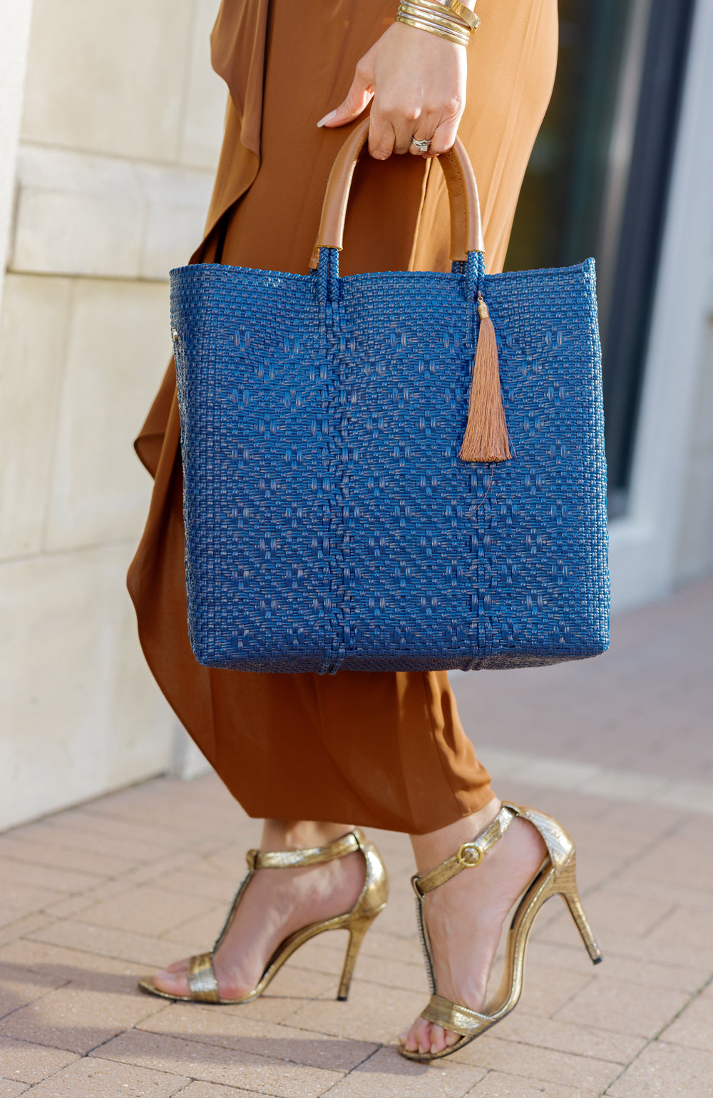Woman in gold dress with heels holding navy blue woven handbag in city setting