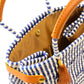 Tan lining inside navy blue and white striped handbag made from woven recycled plastics with brown leather handles, closure straps, and tassel