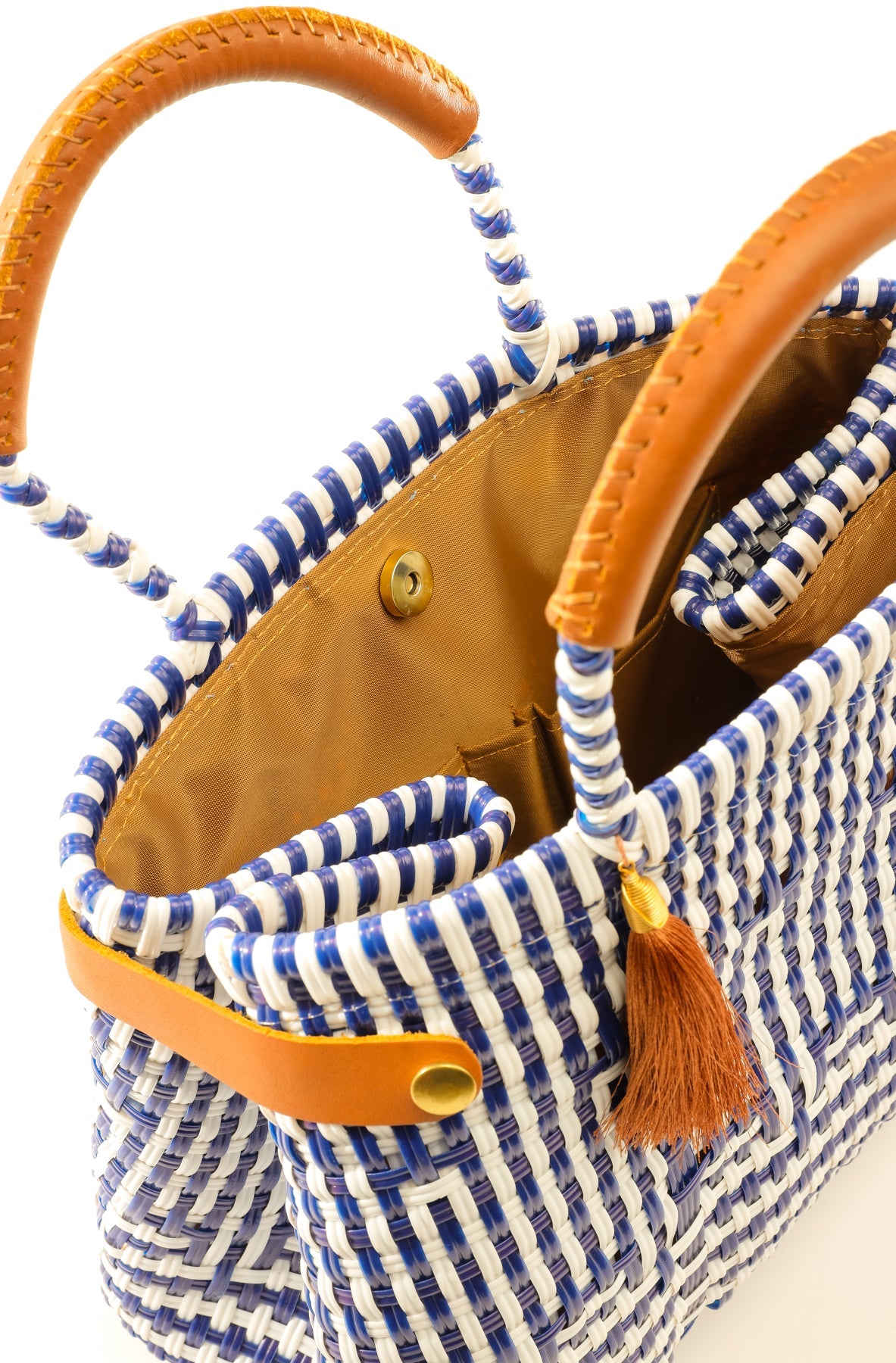 Tan lining inside navy blue and white striped handbag made from woven recycled plastics with brown leather handles, closure straps, and tassel