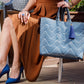 Woman wearing a burnt orange dress and blue heels holding navy blue and white chevron handbag in a city setting