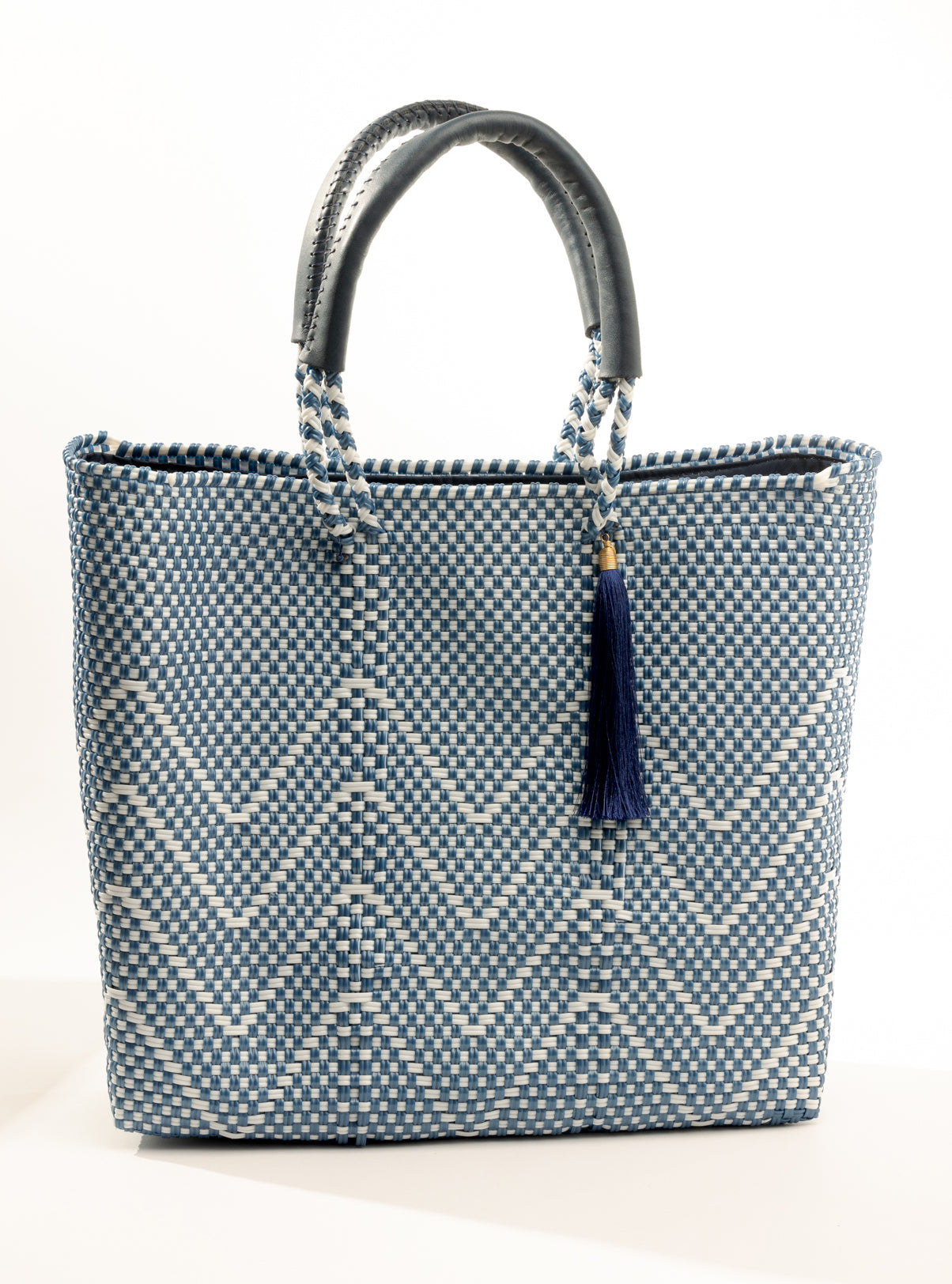 Blue and white chevron woven bucket bag made from recycled plastics featuring navy blue leather handles and tassel detail