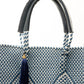 Closeup of fabric of blue and white chevron woven bucket bag made from recycled plastics featuring navy blue leather handles and tassel detail
