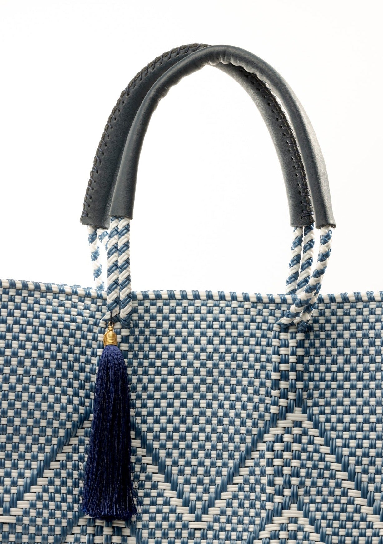 Closeup of fabric of blue and white chevron woven bucket bag made from recycled plastics featuring navy blue leather handles and tassel detail