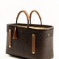 Side angle of brown woven recycled bucket handbag with brown leather handles and closure straps and a brown tassel