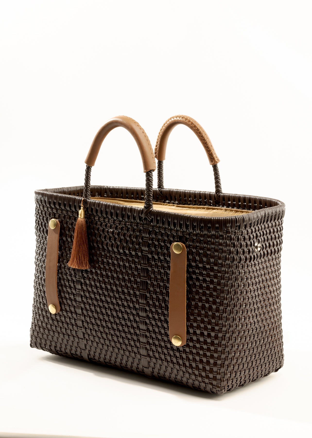 Side angle of brown woven recycled bucket handbag with brown leather handles and closure straps and a brown tassel