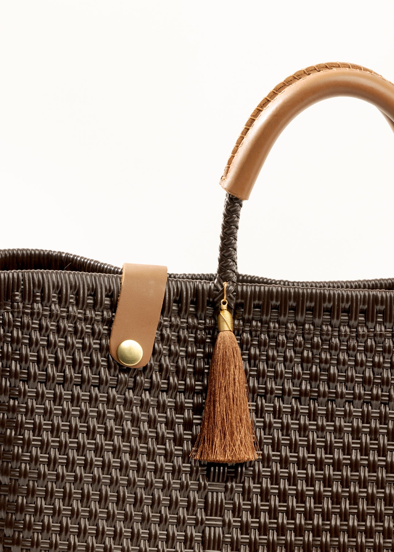 Closeup of brown woven material, leather straps, and tassel on handbag