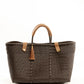 Brown woven recycled bucket handbag with brown leather handles and closure straps and a brown tassel