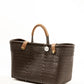 Side angle of brown woven recycled bucket handbag with brown leather handles and closure straps and a silver Coba logo medallion