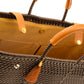 Inside tan fabric lining with two storage pockets and magnetic closure on brown woven handbag with leather handles, closure straps, and tassel detail