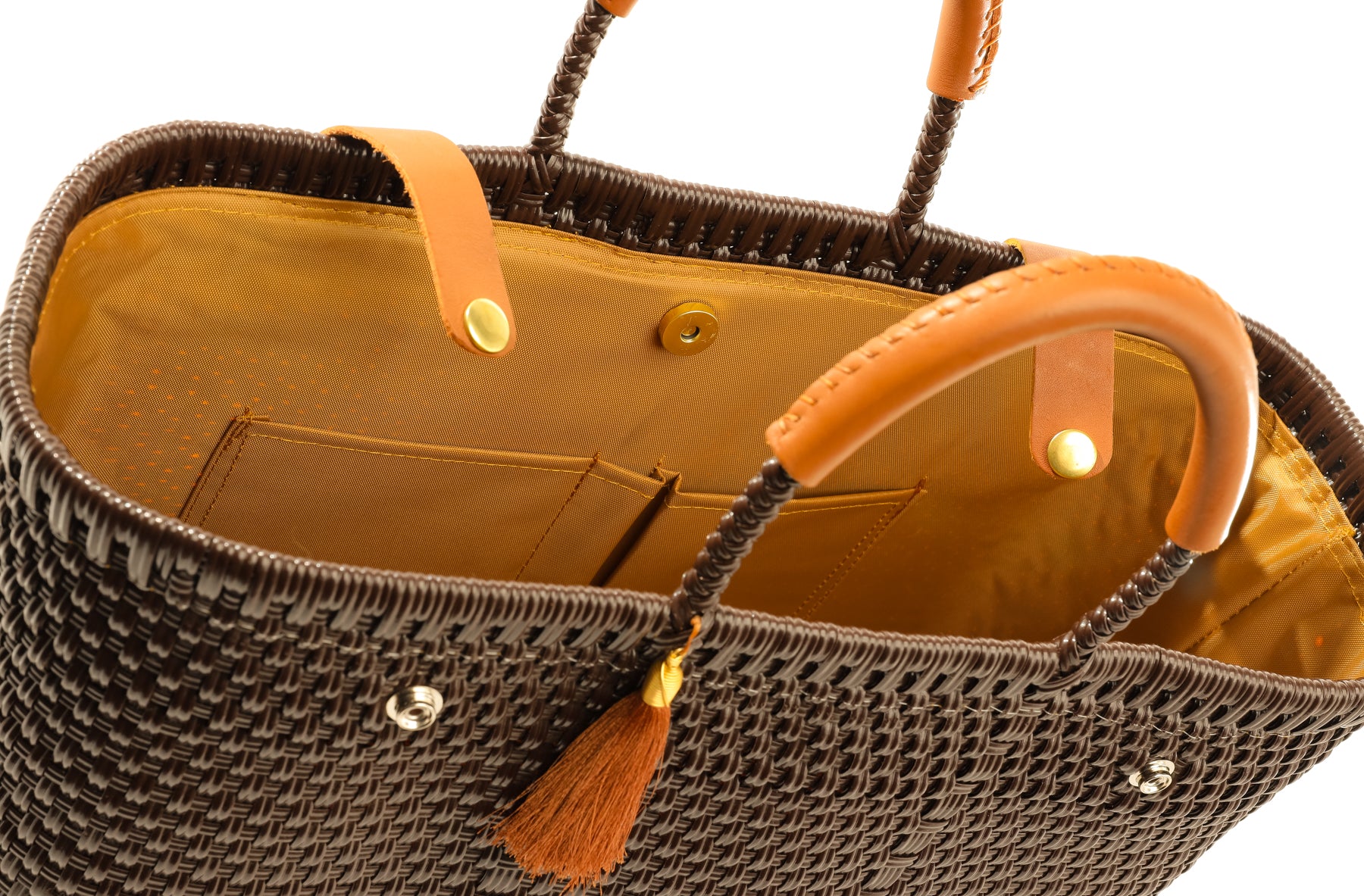 Inside tan fabric lining with two storage pockets and magnetic closure on brown woven handbag with leather handles, closure straps, and tassel detail