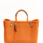 Orange woven handbag with tan leather handle, closure straps, and tassel