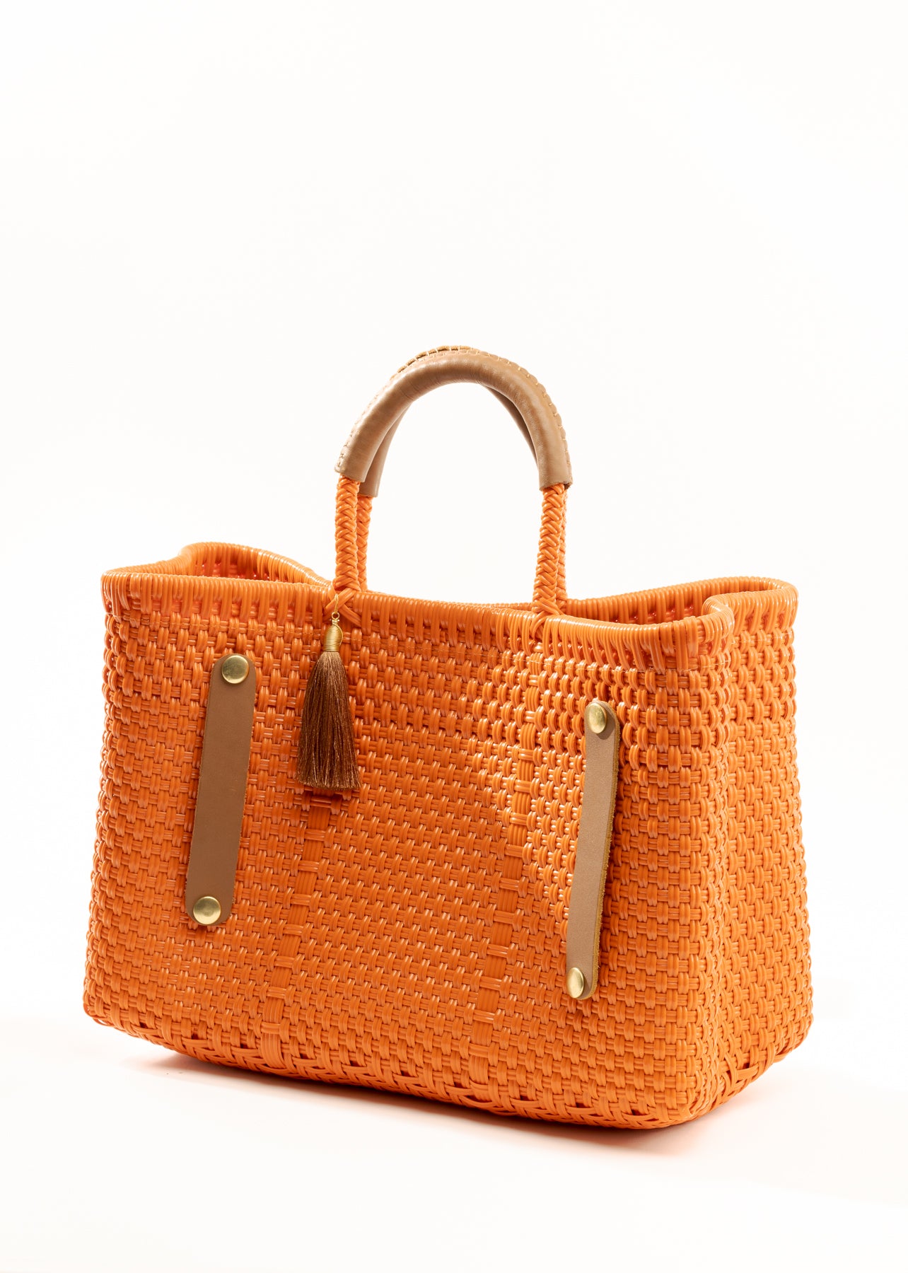Side angle showing orange woven handbag with tan leather handle, closure straps, and tassel