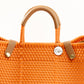 Closeup of woven fabric texture of orange woven handbag with tan leather handle, closure straps, and silver Coba medallion