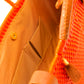 Inside tan lining, pockets, and magnetic closure of orange woven handbag with tan leather handle, closure straps, and tassel