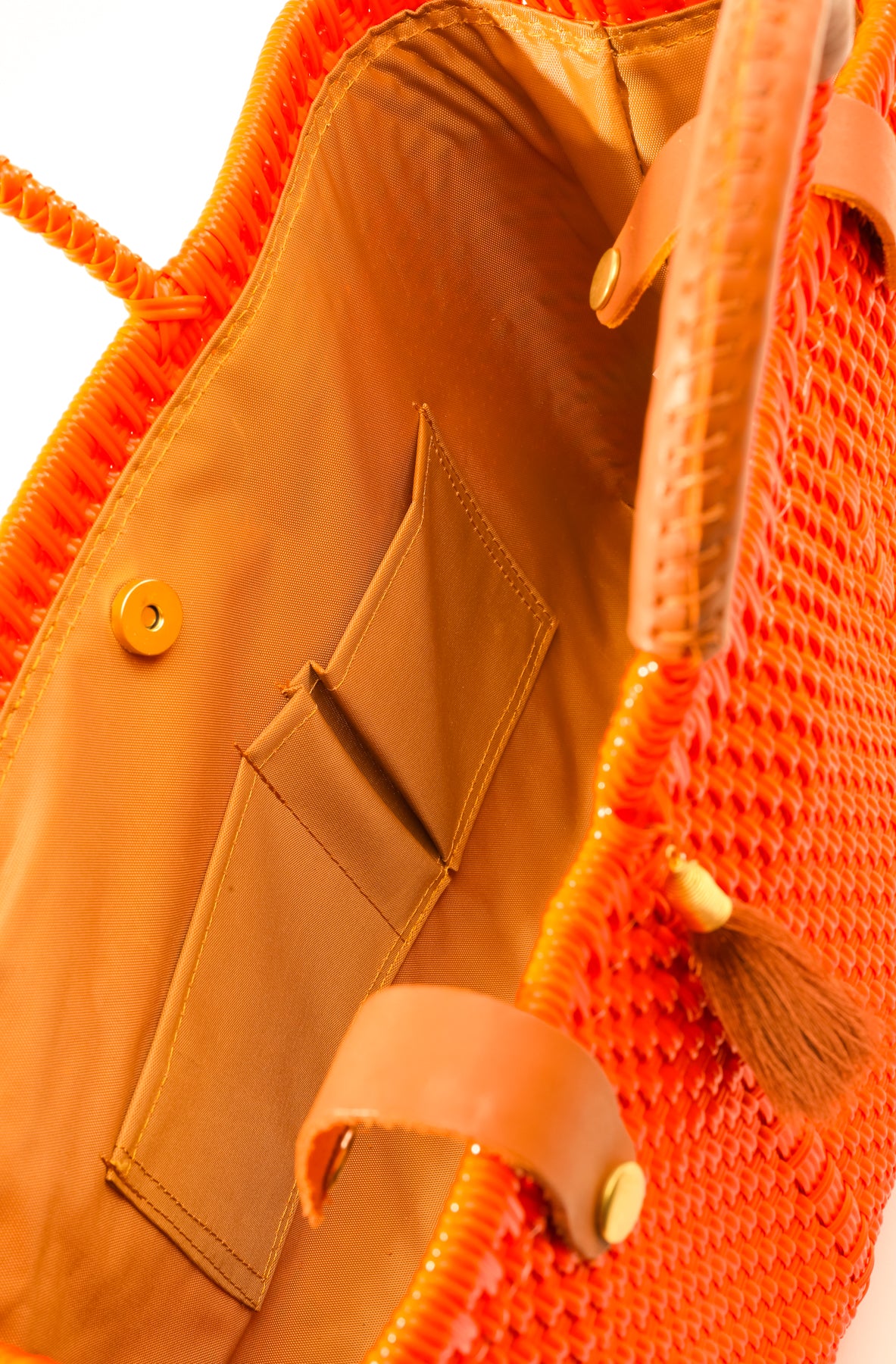 Inside tan lining, pockets, and magnetic closure of orange woven handbag with tan leather handle, closure straps, and tassel