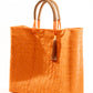 Side angle of orange woven tote bag made from recycled plastics with tan handles and tan tassel detail