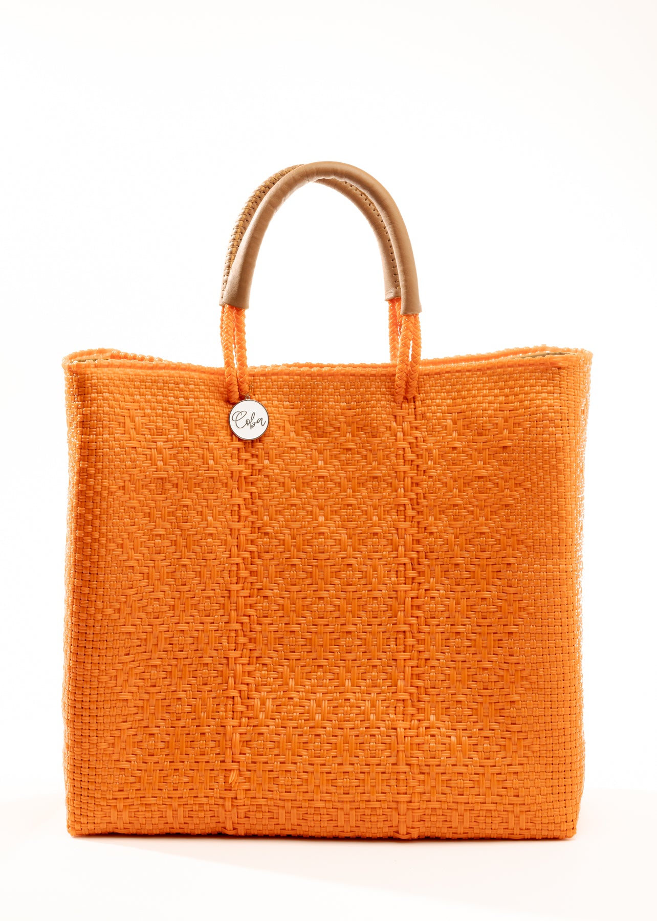 Side angle of orange woven tote bag made from recycled plastics with tan handles and silver Coba logo medallion