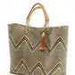 Angle view of a tan, cream, and brown chevron tote bag made from recycled plastics featuring a tan leather handle and tassel detail