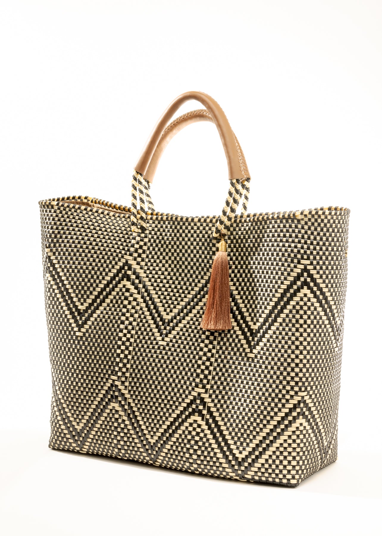 Angle view of a tan, cream, and brown chevron tote bag made from recycled plastics featuring a tan leather handle and tassel detail