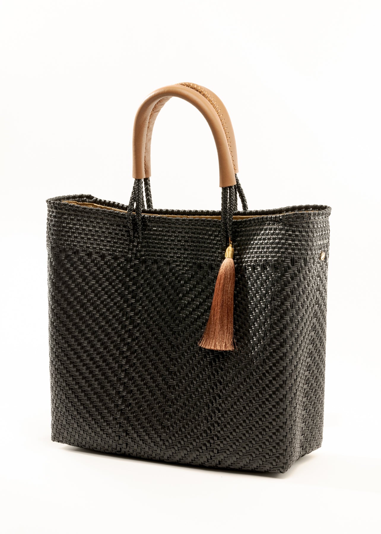 Side angle view of black and brown woven bucket bag made from recycled plastics featuring tan leather handles and tassel detail