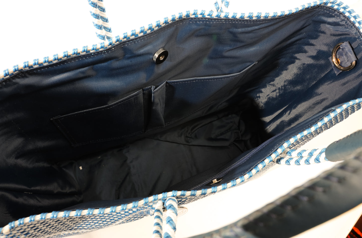 Inside navy blue lining featuring 2 pockets and magnetic closure of blue and white chevron woven bucket bag made from recycled plastics featuring navy blue leather handles and tassel detail
