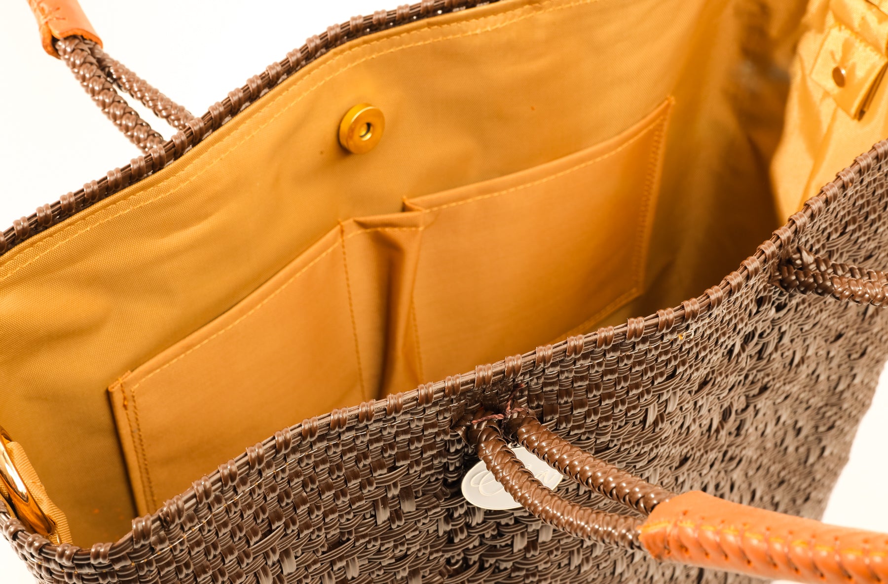 Inside tan lining with two pockets and magnetic closure of brown and tan woven handbag made from recycled plastics