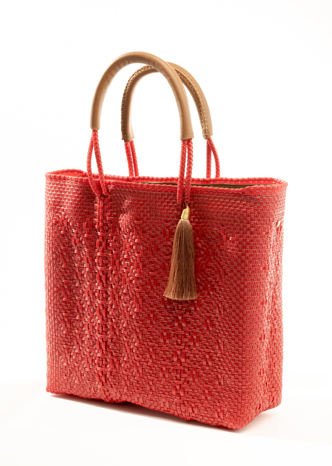 Angled view of red woven bucket bag made from recycled plastics with tan leather handle and tassel