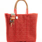 Red woven bucket bag made from recycled plastics with tan leather handle and silver Coba logo medallion and multi colored strap draped over the bag