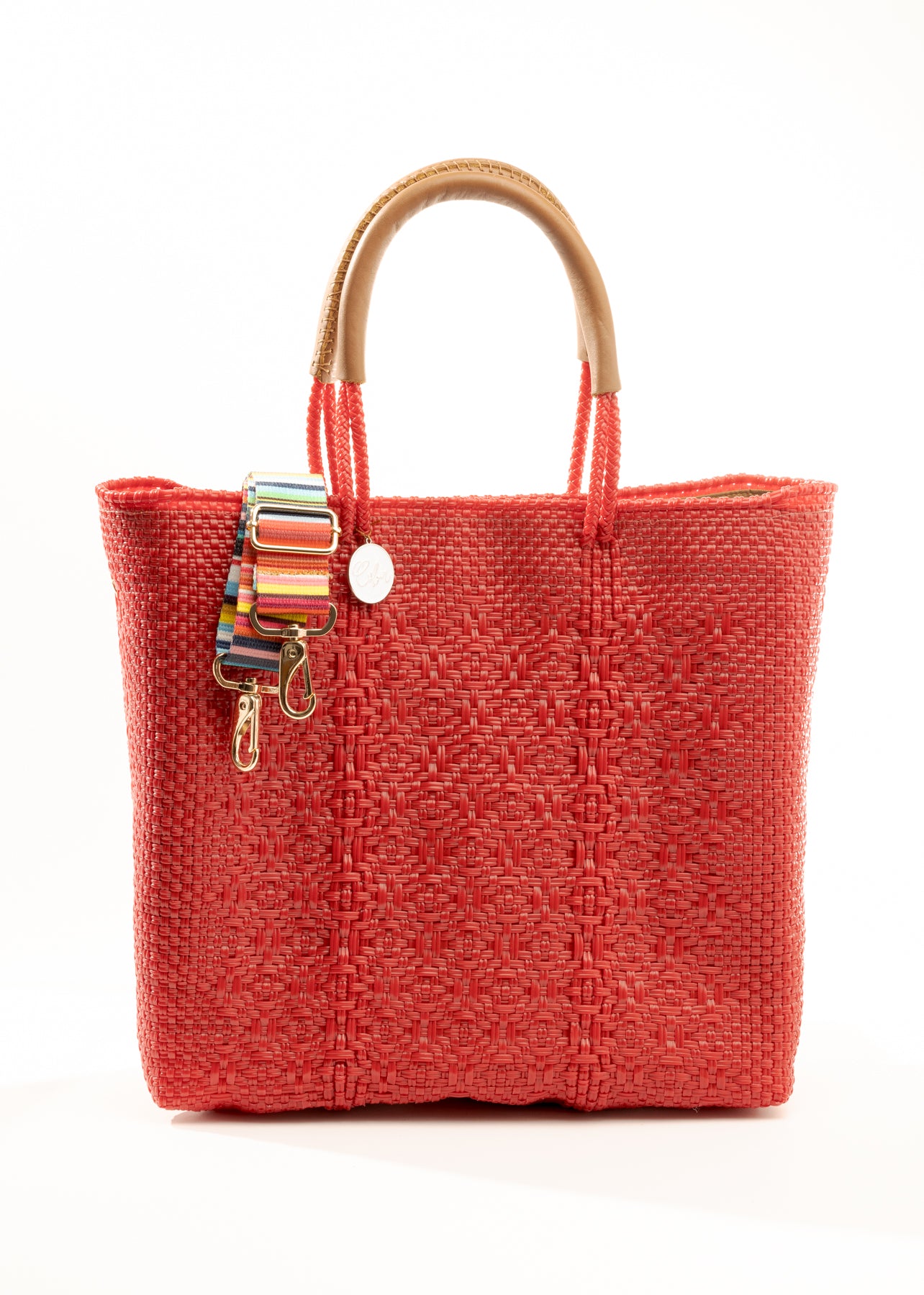 Red woven bucket bag made from recycled plastics with tan leather handle and silver Coba logo medallion and multi colored strap draped over the bag
